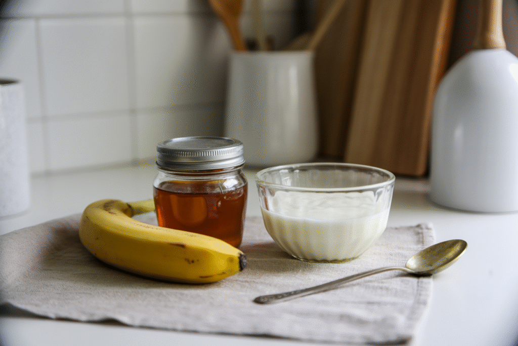 Ingredients for a DIY hair mask with banana, honey, and yogurt on a neutral background.
